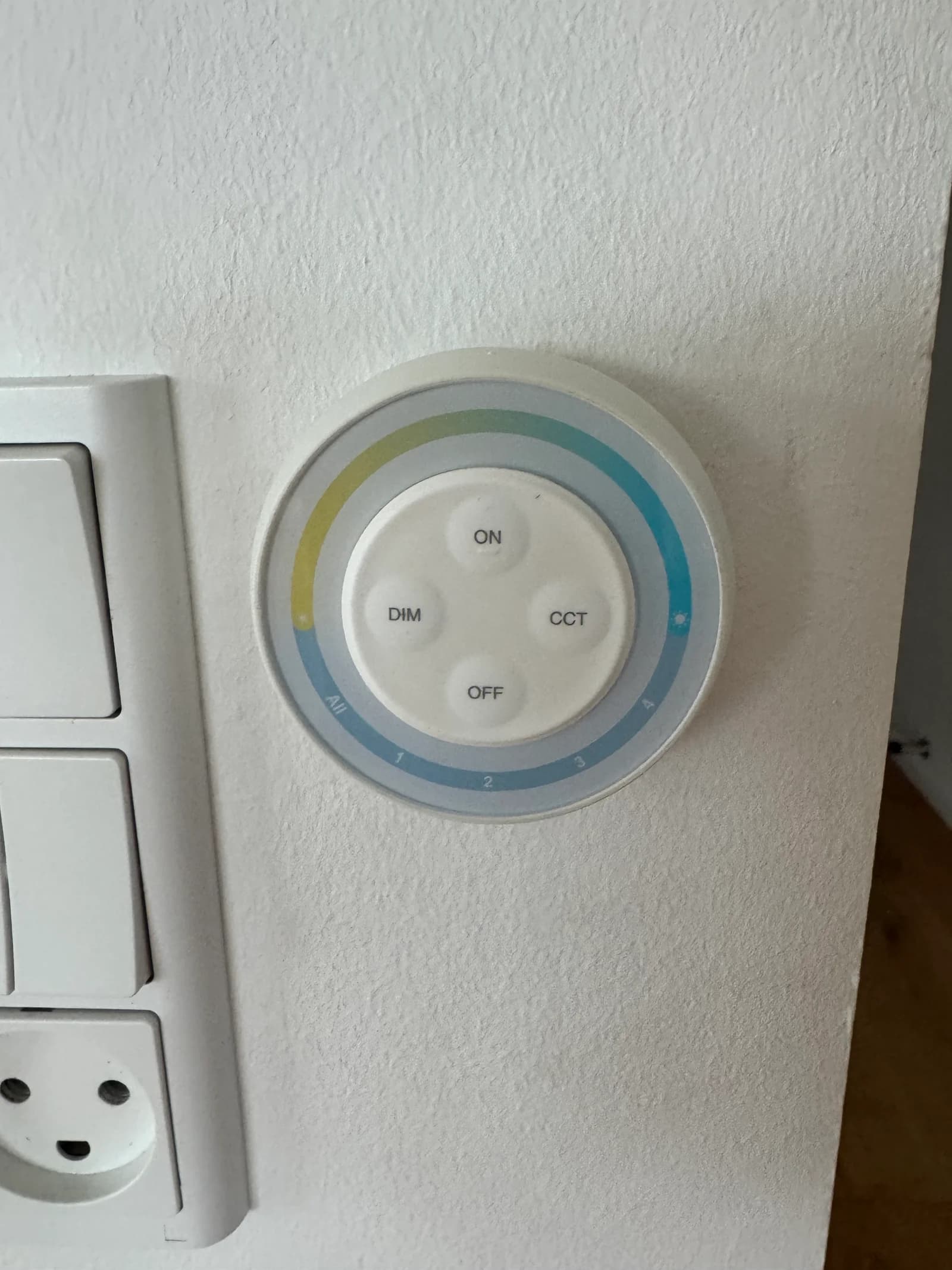 Round lighting controller beside the wall switches, with All on the lower-left edge and ON, OFF, DIM and CCT in the centre